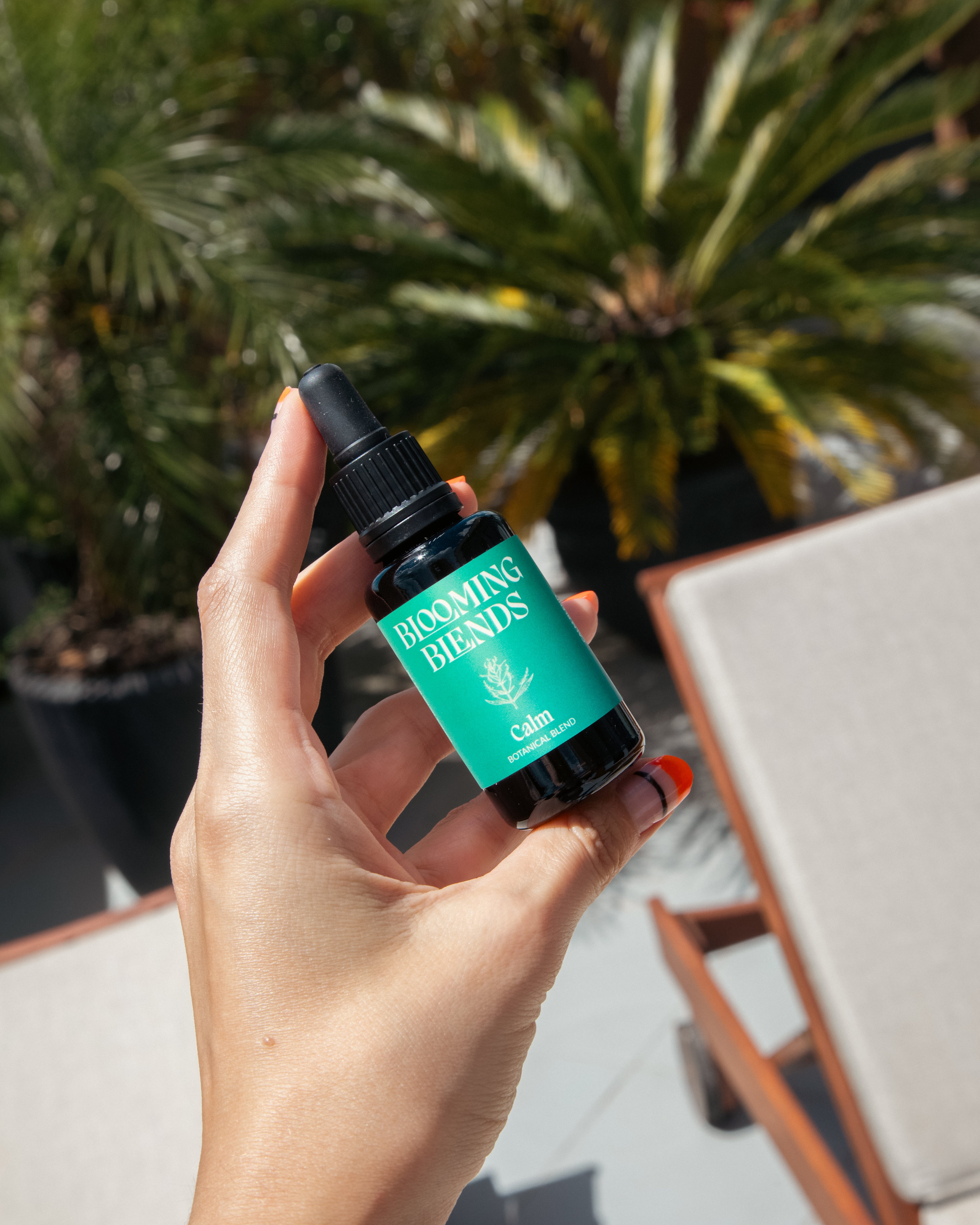 Hand holding a Blooming Blends Calm herbal tincture bottle outdoors.
